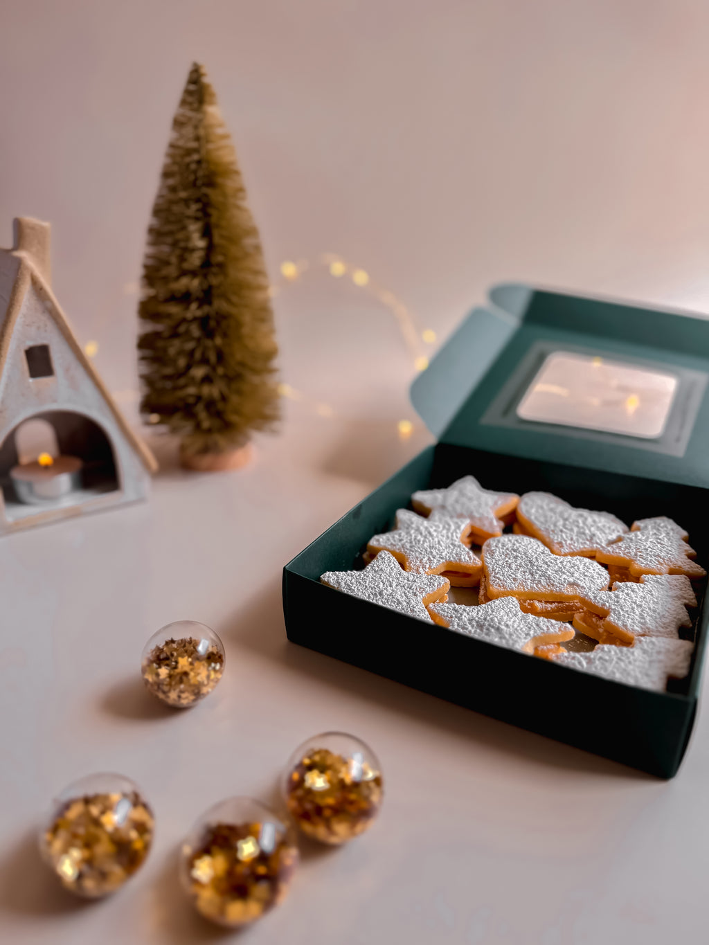Box of alfajores/cookies filled with dulce de leche and with powdered sugar, Christmas decorations on a table