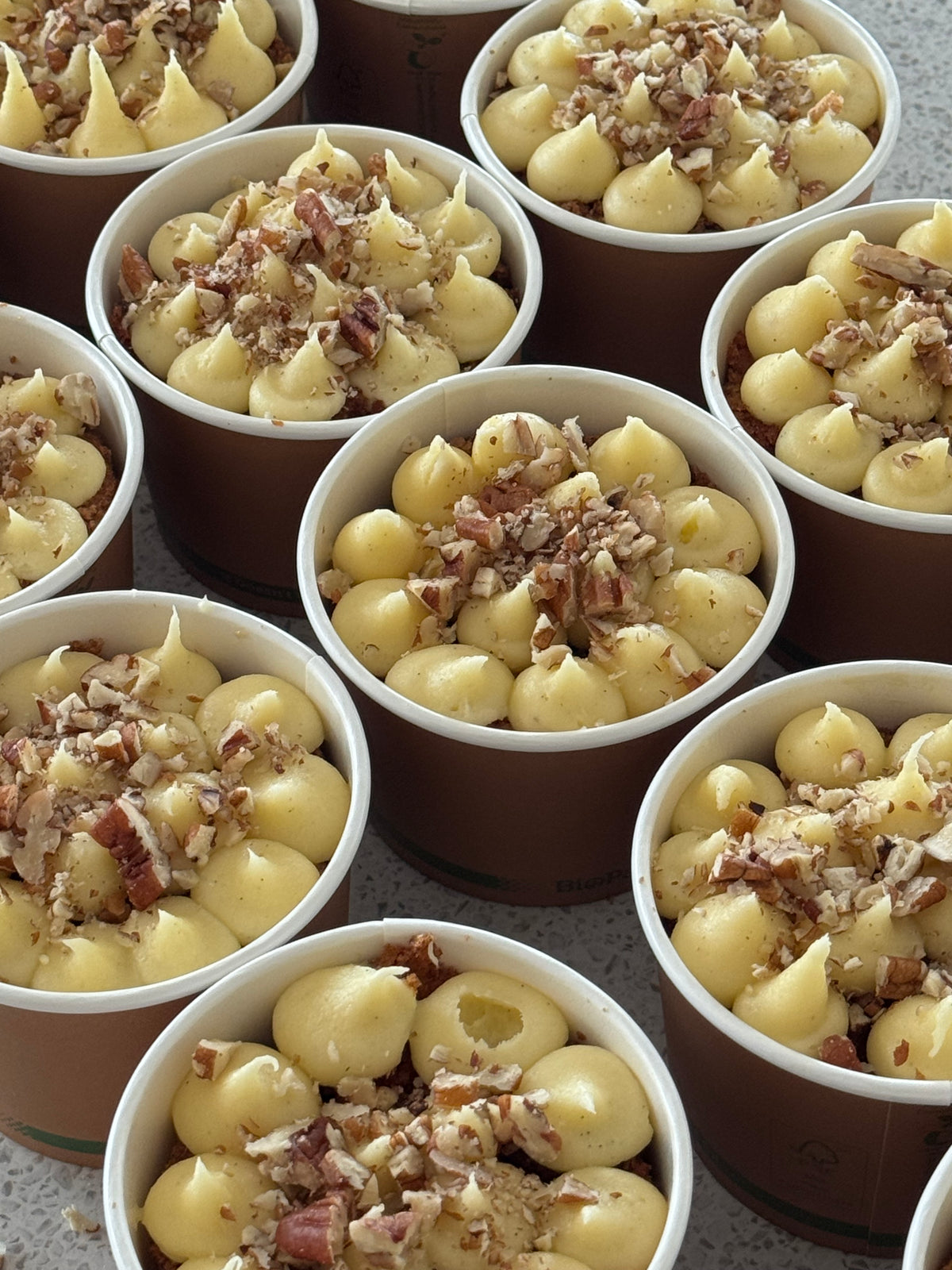 Carrot cake dessert cups topped with cream cheese buttercream, pecans and dulce de leche, arranged together in paper cups.