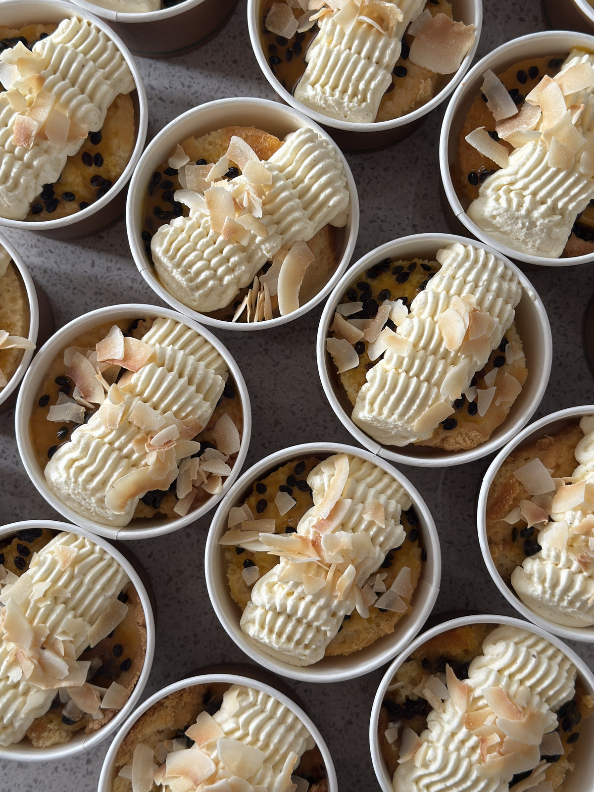 Passionfruit and coconut tres leches dessert cups topped with whipped cream, passionfruit sauce and coconut flakes.